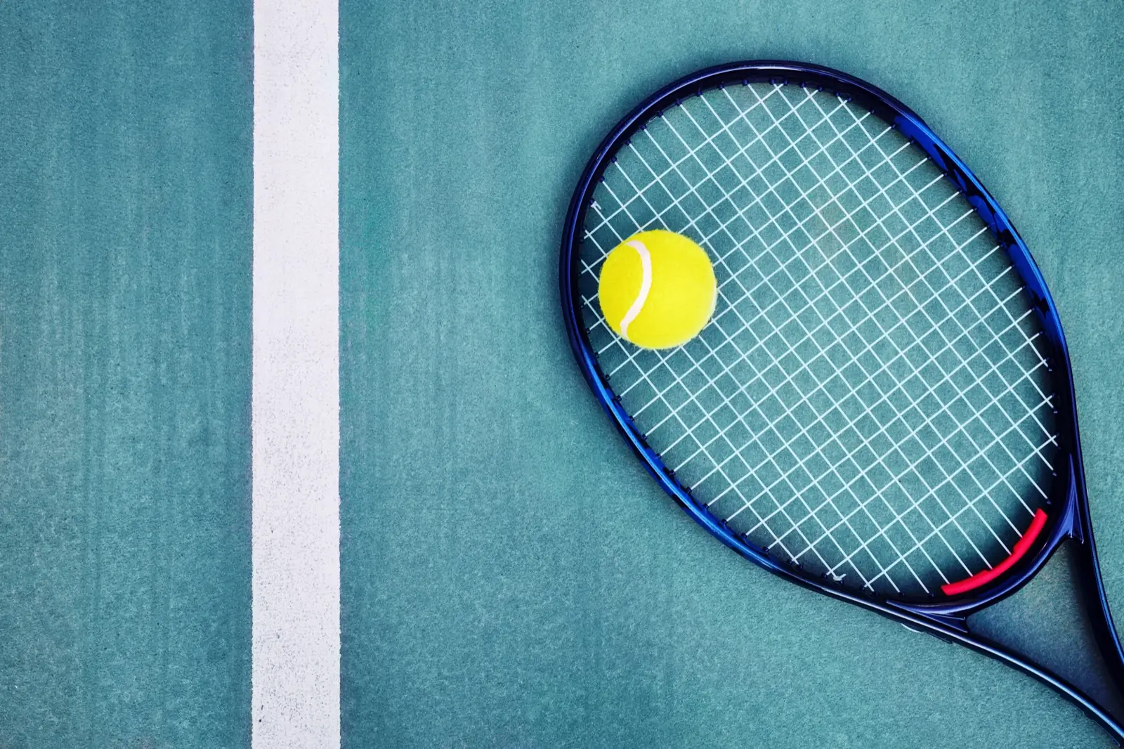 Racchetta e pallina da tennis su un campo in cemento